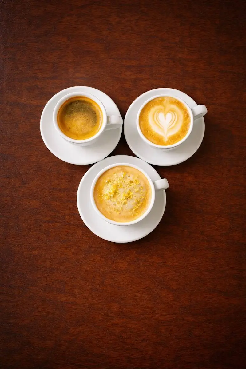 three cups of coffee with latte art on wooden table at Kings Afro Barbershop in JVC Dubai