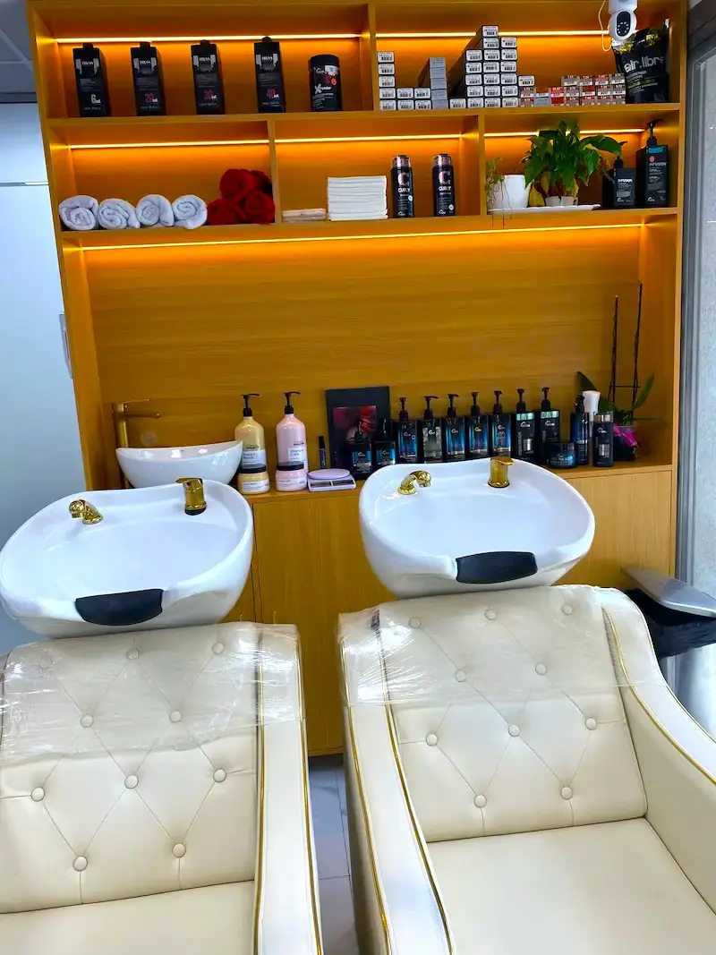 modern barbershop hair washing stations with two shampoo chairs and sinks, shelves with hair products and warm ambient lighting
