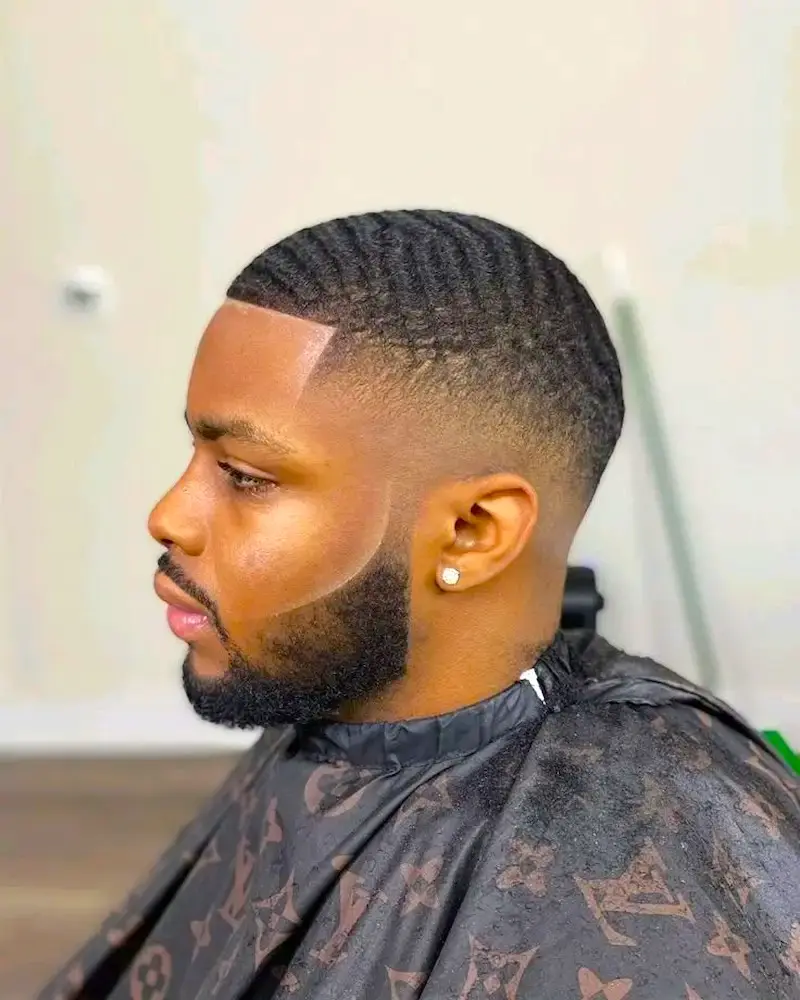 man with clean fade haircut and styled beard side profile in barber chair professional grooming result
