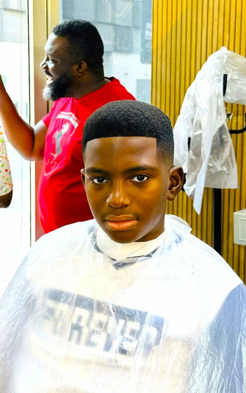 young boy after a fresh haircut sitting in a barber chair with a clean low fade and sharp lineup inside a modern barbershop
